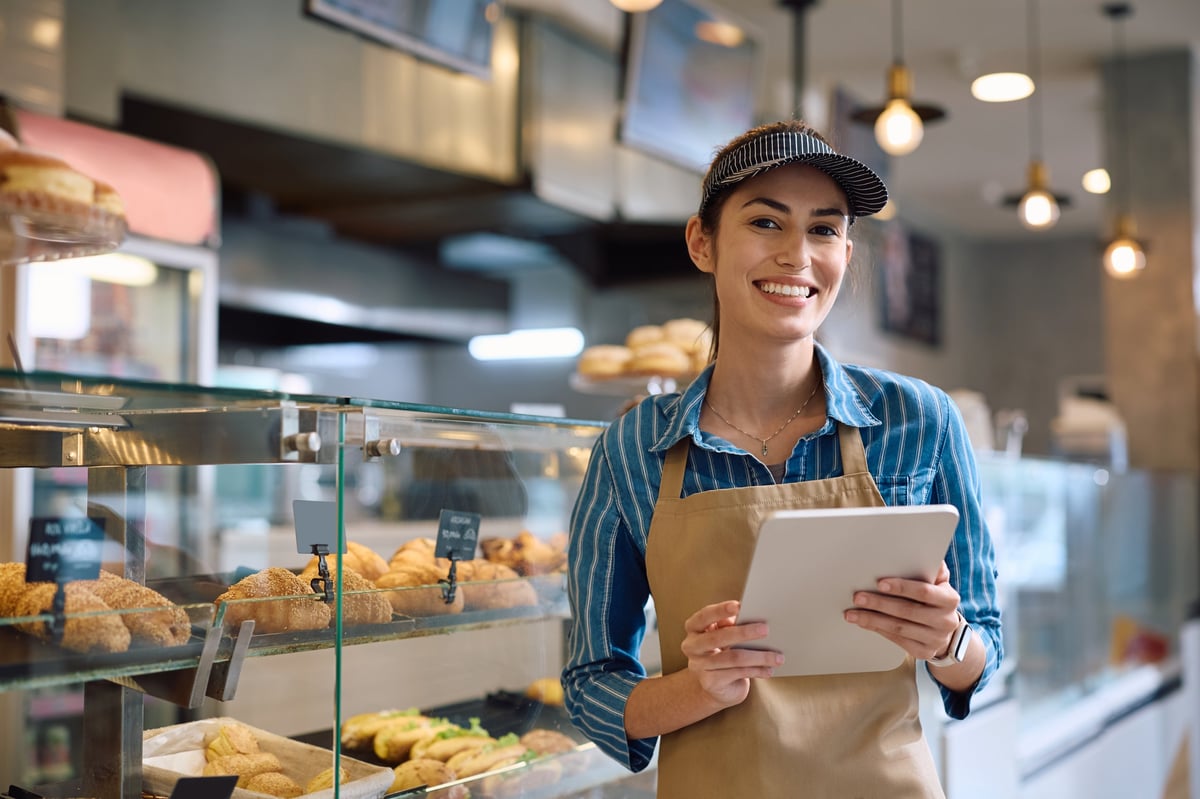 Happy female bakery worker using tablet in small business