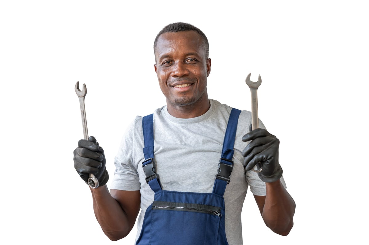 Happy African American male auto mechanic in overalls holding wrenches ready for work