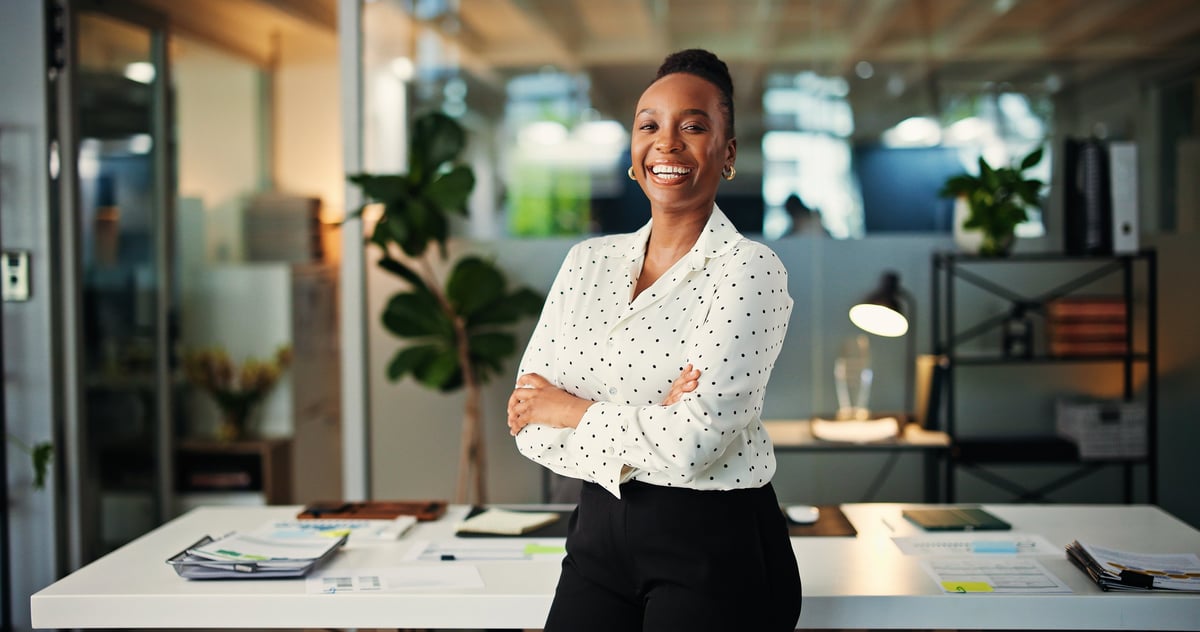 Confident Black businesswoman with arms crossed smiling in modern office